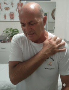 גבר אוחז בכתפה בכאב, ברקע סביבה ביתית רגועה